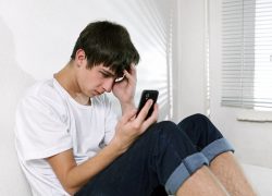 Zestresowany nastolatek siedzi na podłodze i patrzy w telefon