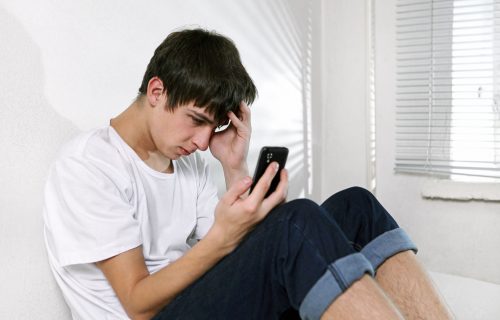 Zestresowany nastolatek siedzi na podłodze i patrzy w telefon